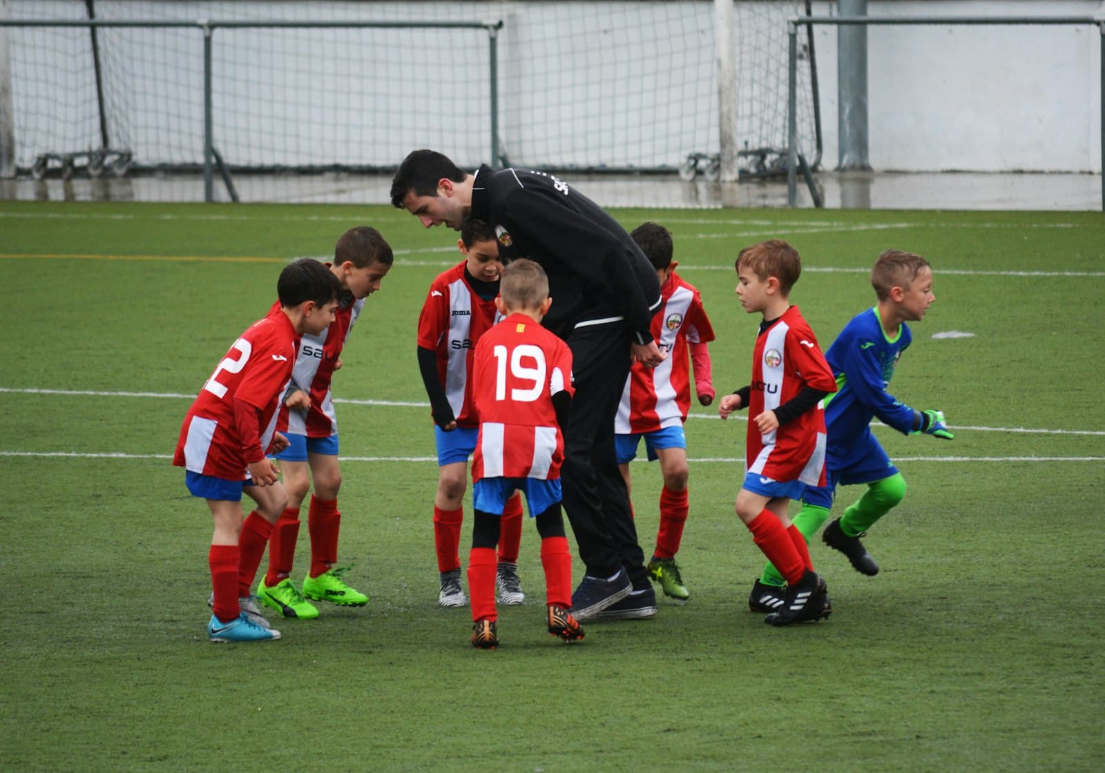 A coach huddled with a young football team, guiding the players on the pitch