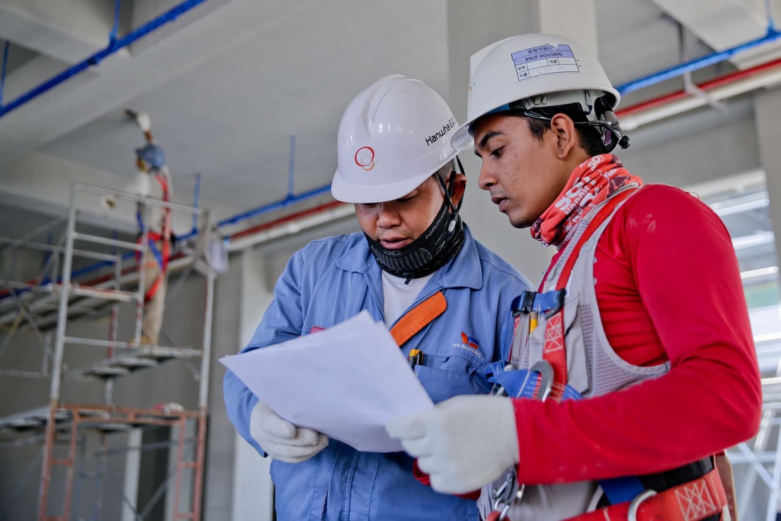 Two site workers in hard hats reviewing plans together